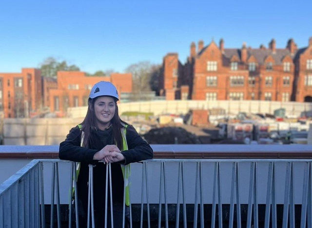 Orláigh Rice wearing a hard hat standing on a balcony with a construction site in behind her